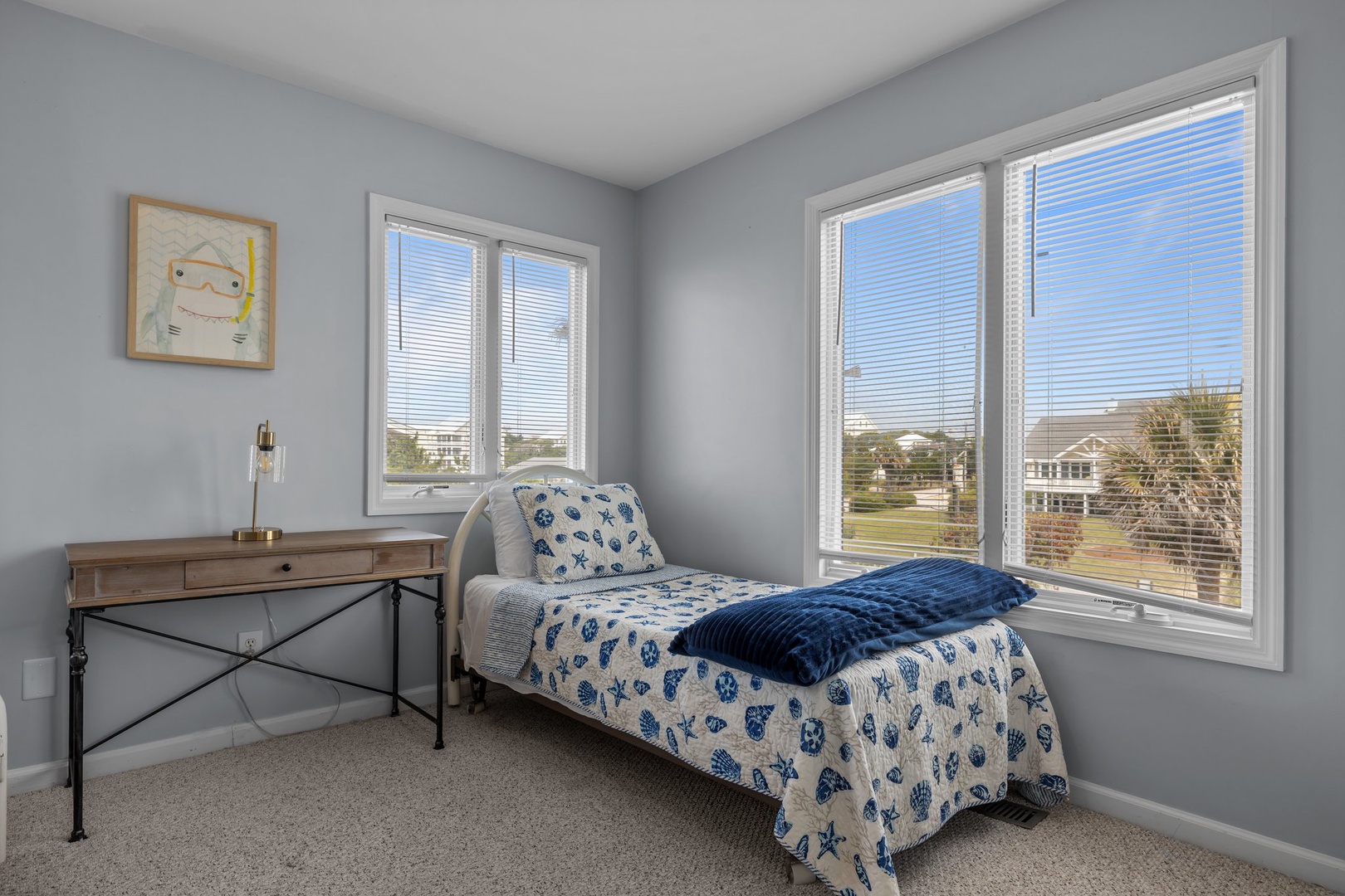 Your peaceful guest room offers morning light through large windows, a cozy single bed with cheerful nautical bedding, and workspace for planning coastal adventures.
