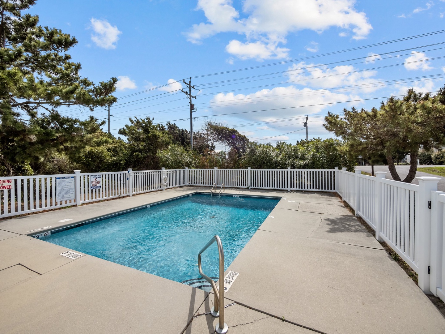 Dive into crystal-clear waters in your private fenced pool, surrounded by lush trees under bright blue skies for perfect relaxation.