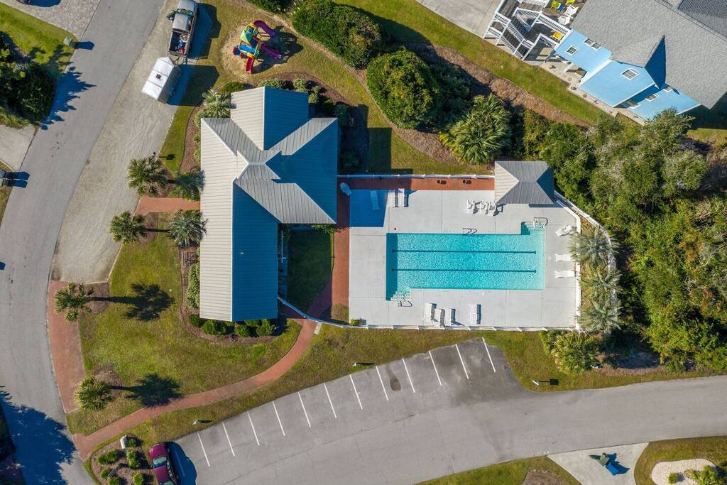 Aerial view of a vacation rental property featuring a large swimming pool surrounded by tropical landscaping and ample parking.