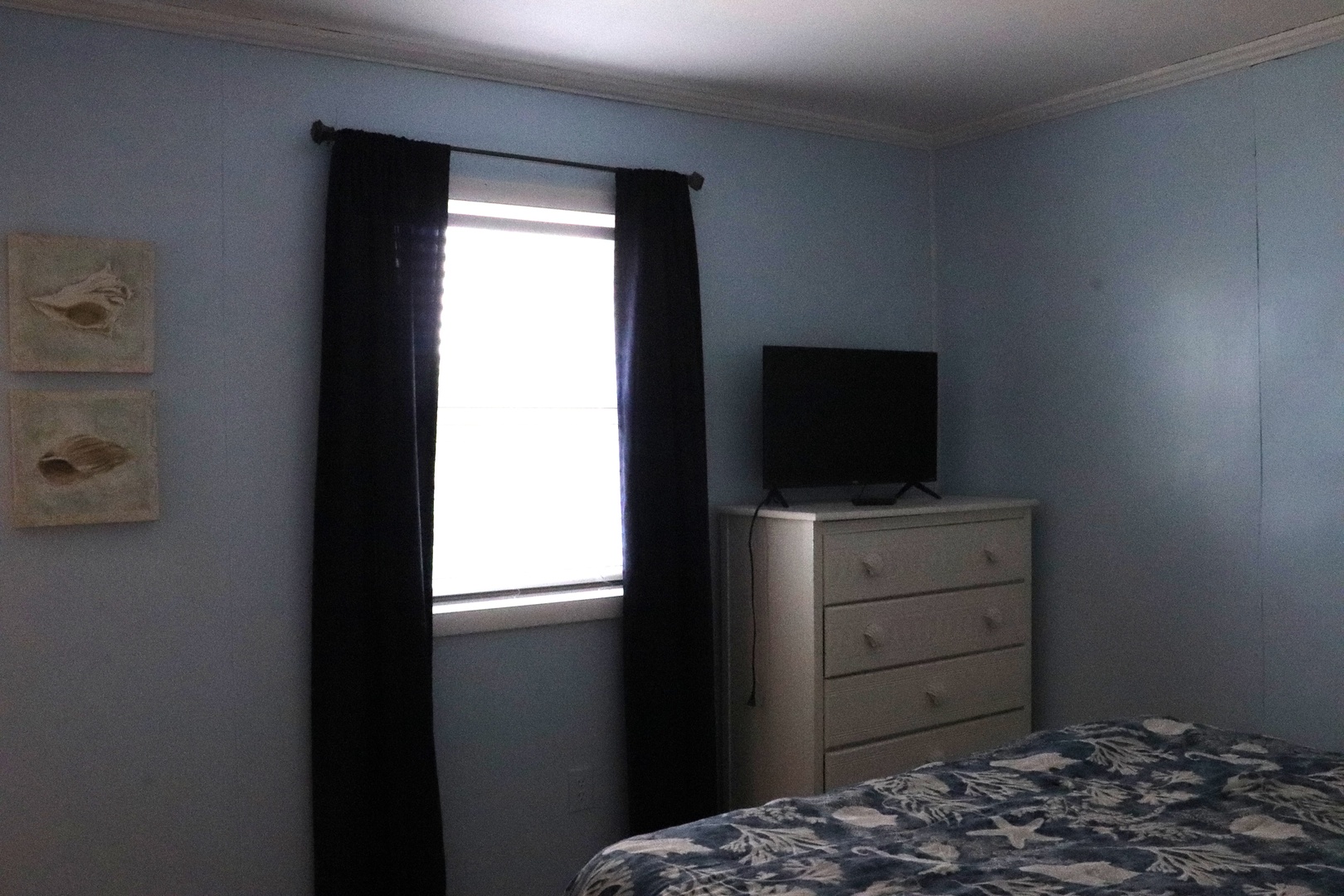 Unwind in this serene bedroom with calming blue walls, natural light filtering through blackout curtains, and a smart TV for your entertainment at day's end.