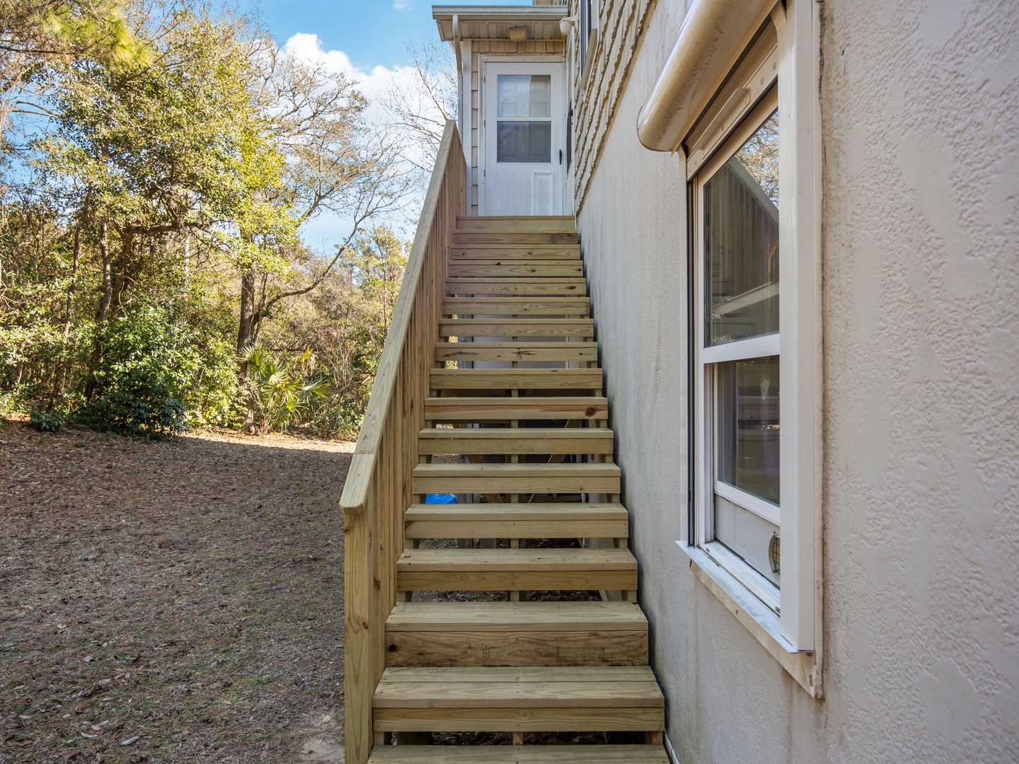 Wooden stairs lead to your private upper-level entrance, surrounded by mature trees in a peaceful residential setting.