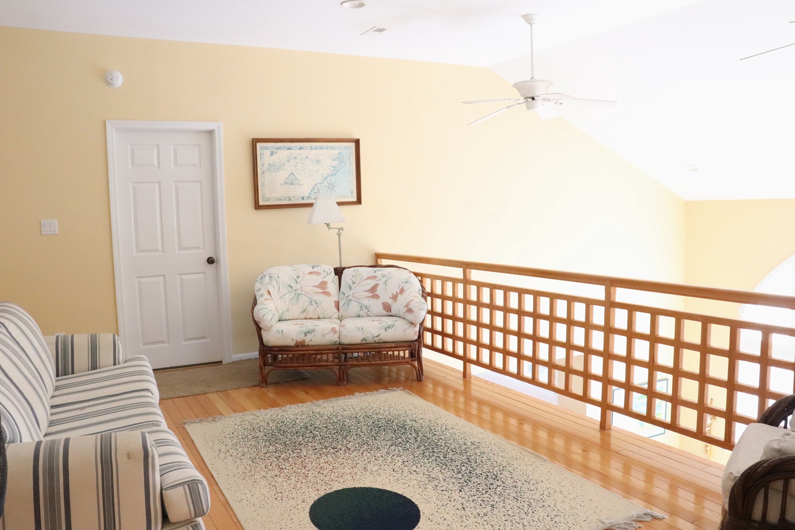 Relax in your upstairs sitting area with coastal charm, where warm yellow walls and wicker seating create a peaceful retreat.