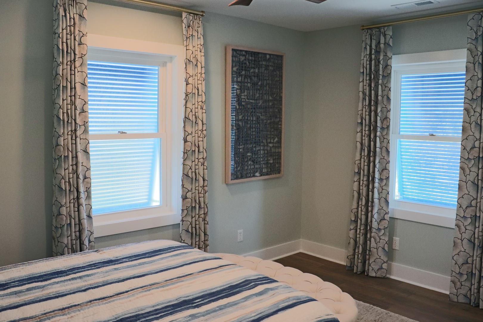 Rest easy in your tranquil bedroom, where soft morning light filters through elegant patterned curtains and peaceful blue-striped bedding awaits.