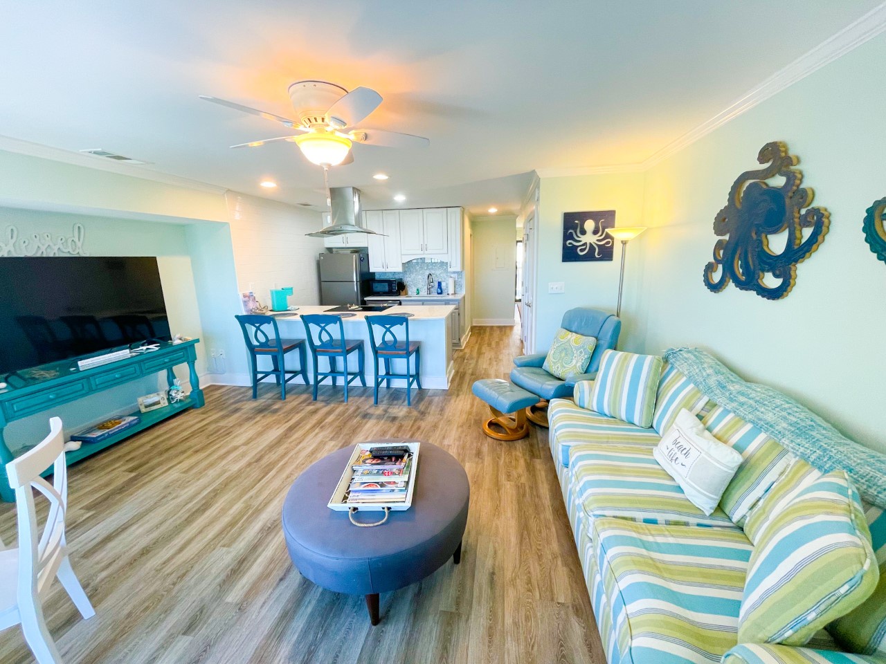 Relax in your coastal-themed living space with ocean-inspired décor, comfy striped sofa, and open kitchen perfect for your vacation meals.