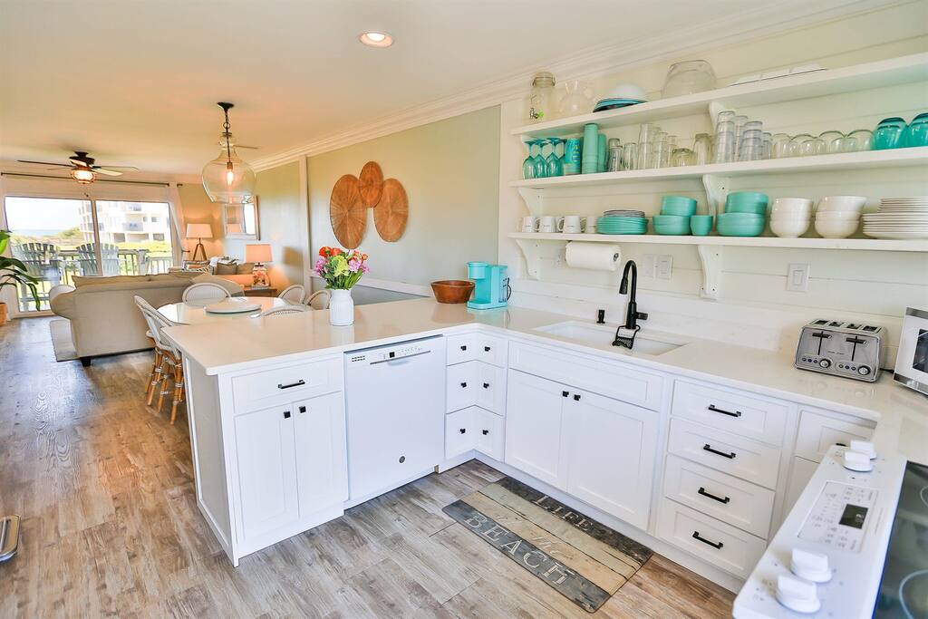 Bright coastal kitchen with turquoise accents and open shelving where you can prepare meals with ocean breeze flowing through.