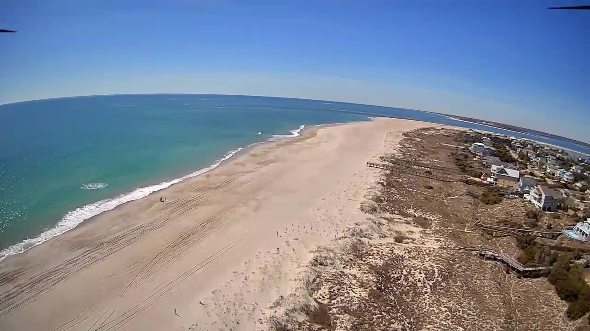 Stunning aerial view captures pristine coastline with expansive sandy beach, crystal-clear waters, and charming coastal community.