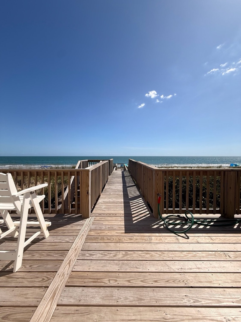 A wooden boardwalk leads directly from the property to pristine sandy shores and sparkling ocean waters—your private pathway to endless beach days under a clear blue sky.