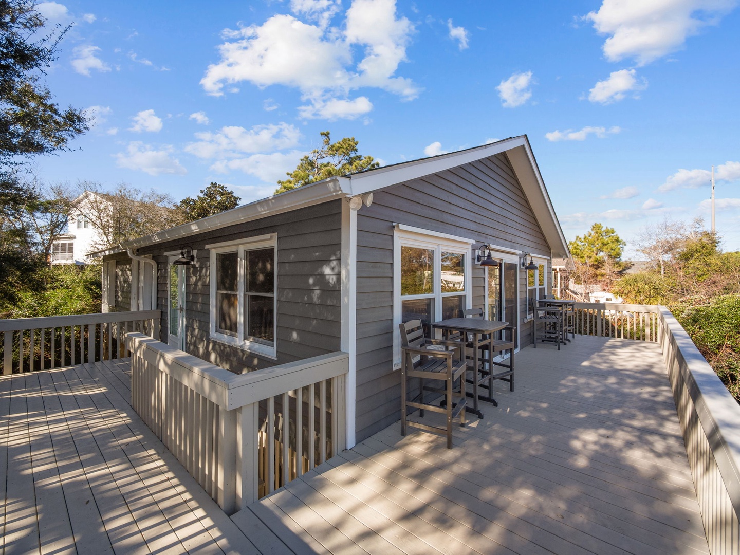 Charming coastal cottage with expansive wraparound deck featuring outdoor seating where you can savor morning coffee or evening cocktails surrounded by mature trees.
