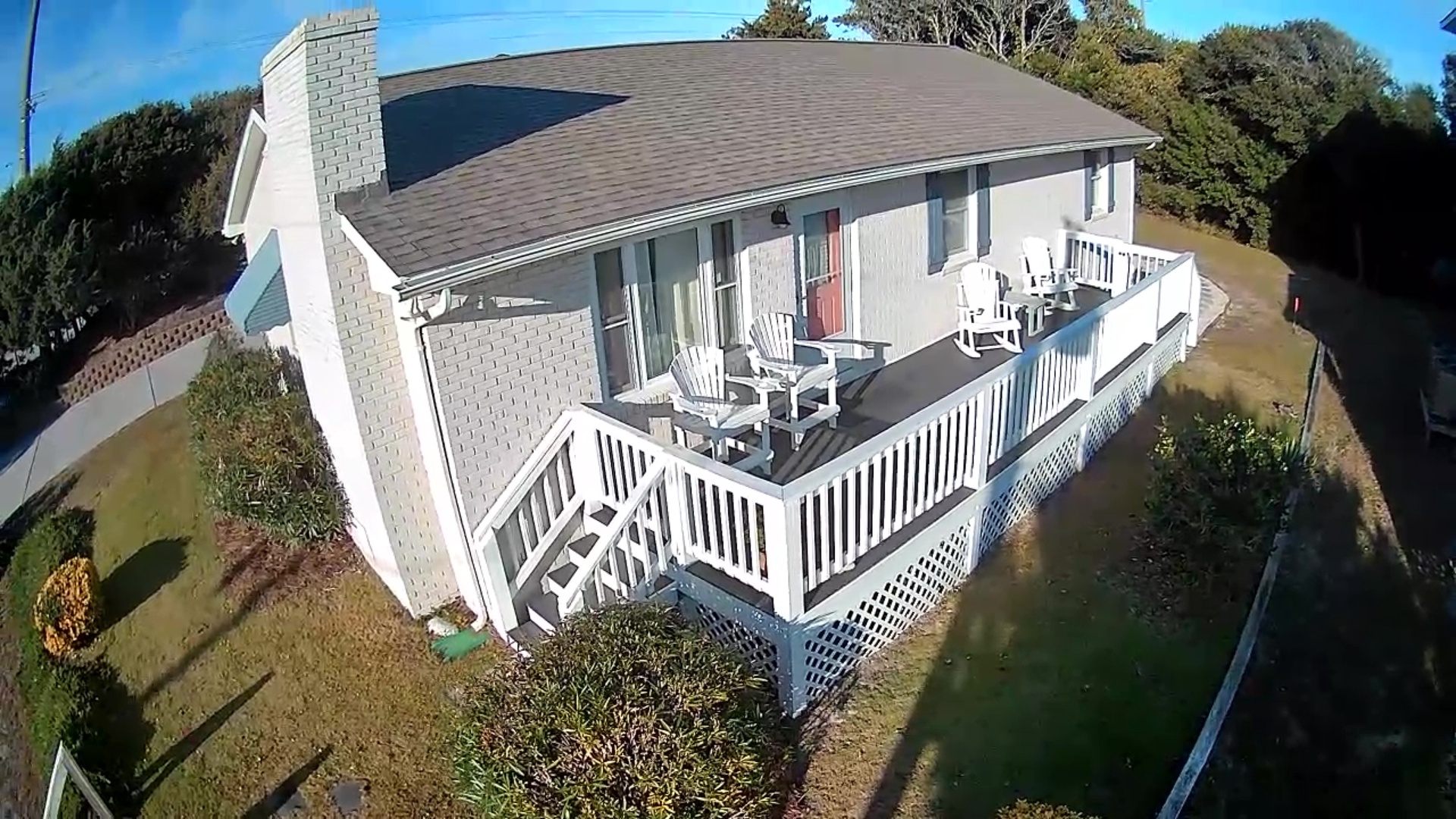 Aerial view of charming vacation rental with spacious wraparound deck and mature landscaping in quiet residential setting.