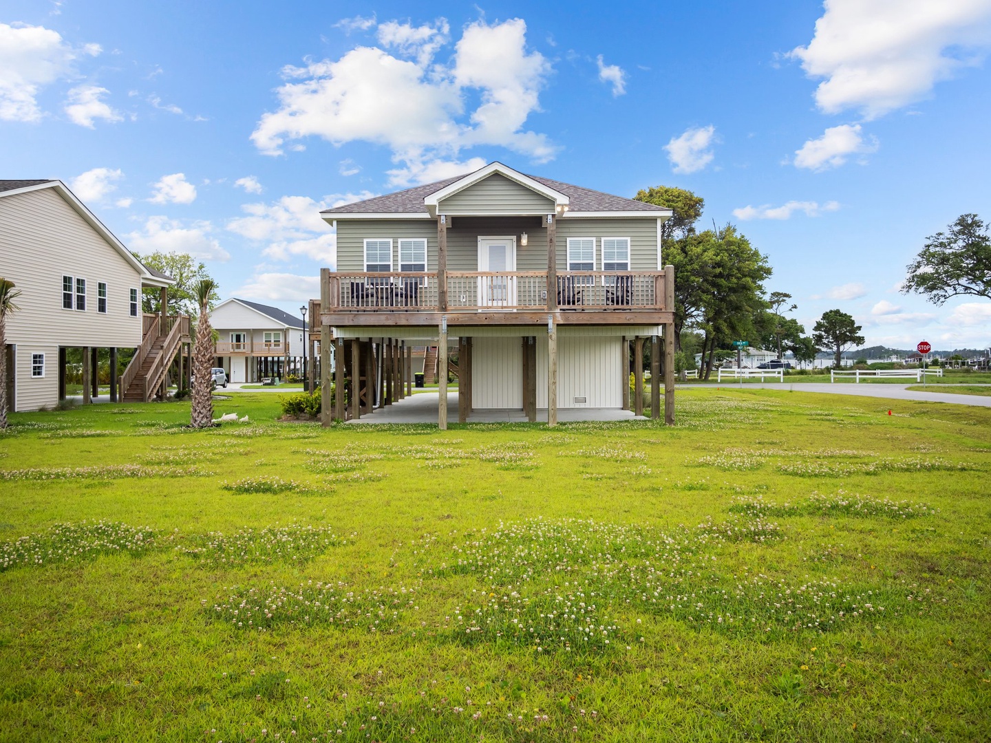 Elevated coastal home with spacious deck and open lawn, surrounded by peaceful neighborhood setting.