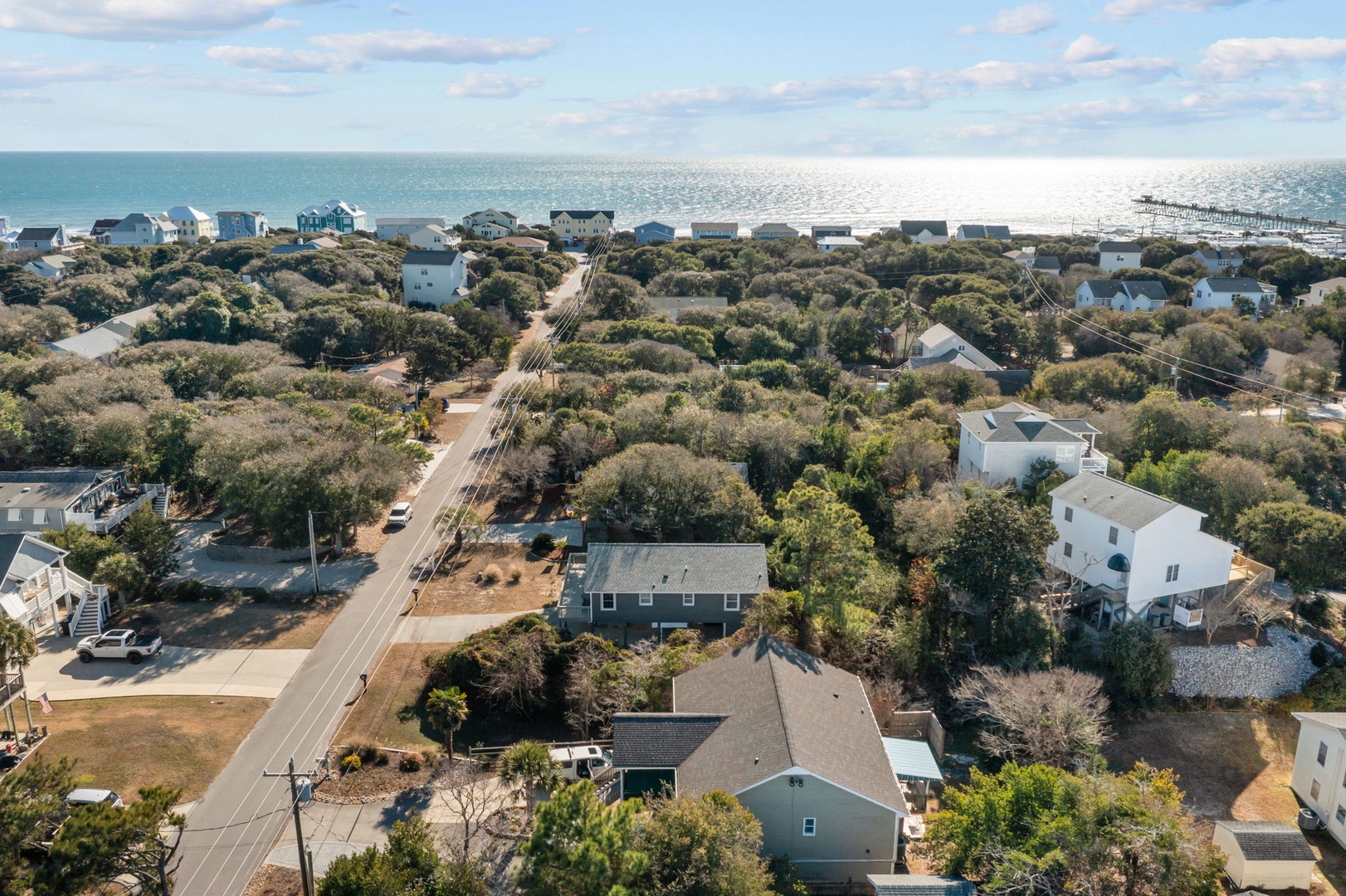 Aerial view of a charming coastal neighborhood with tree-lined streets leading to pristine beachfront homes and sparkling ocean waters.