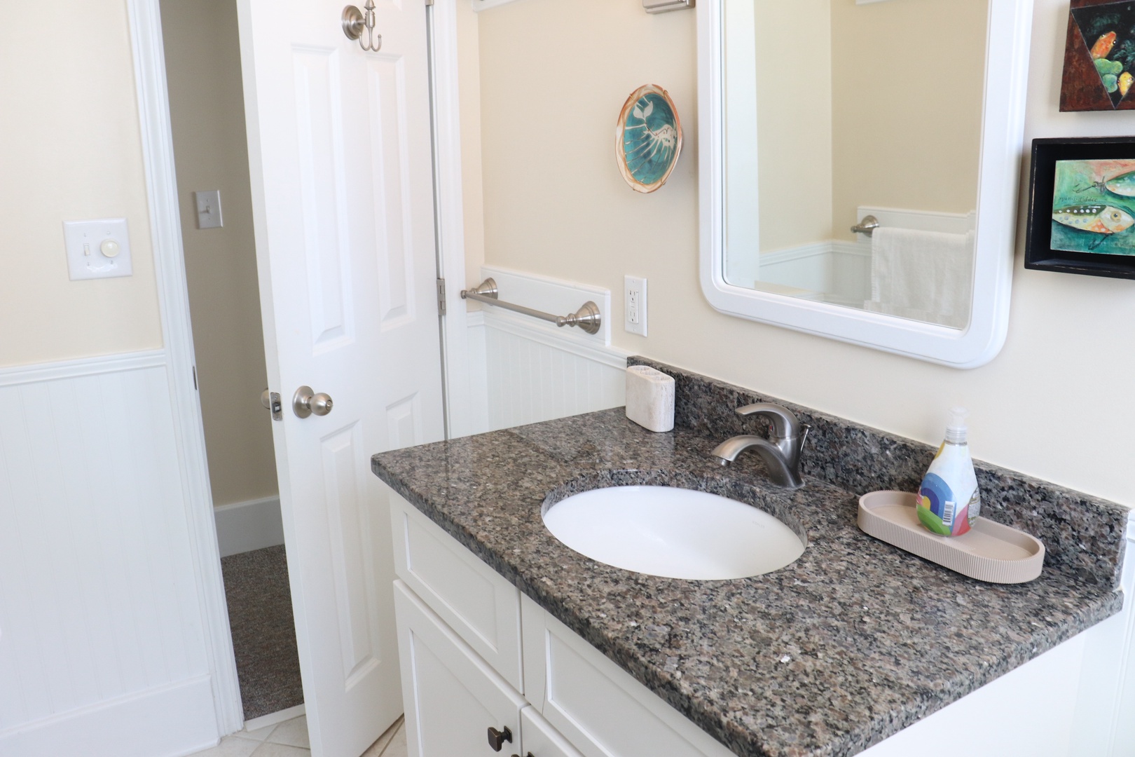 Refresh in your bright bathroom featuring granite countertops and coastal artwork that creates a serene morning routine.