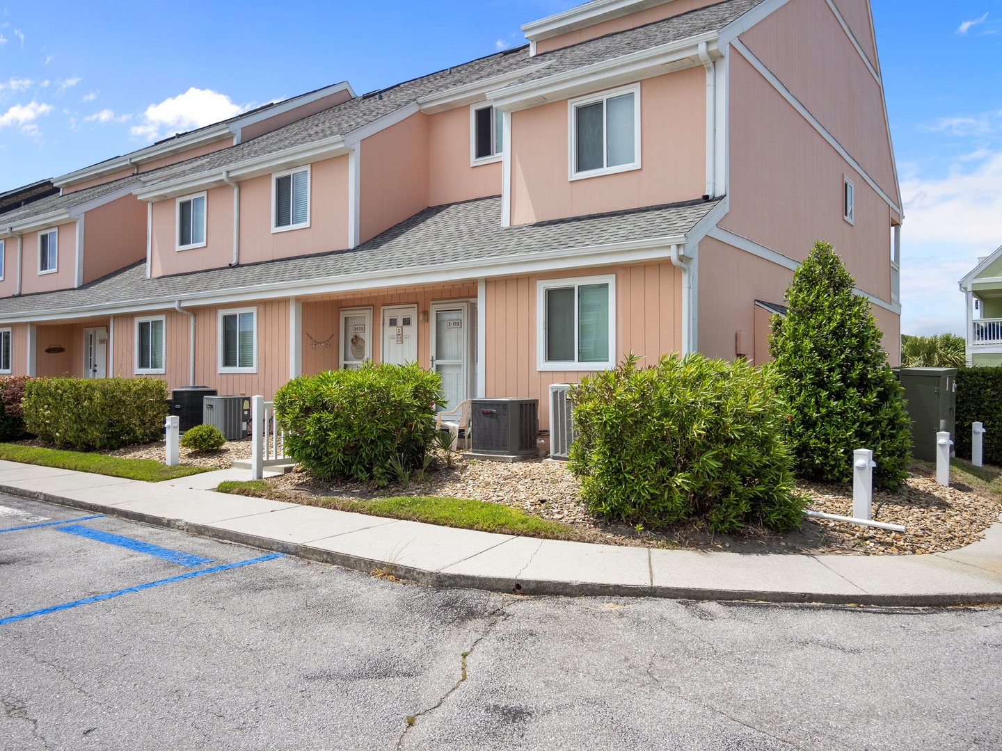 Charming coral-colored townhomes with manicured landscaping and convenient parking spaces in a peaceful residential setting.