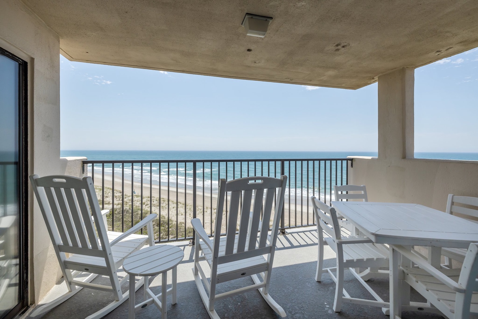 Your private oceanfront balcony awaits with dining table and rocking chairs, where morning coffee meets endless sea views.