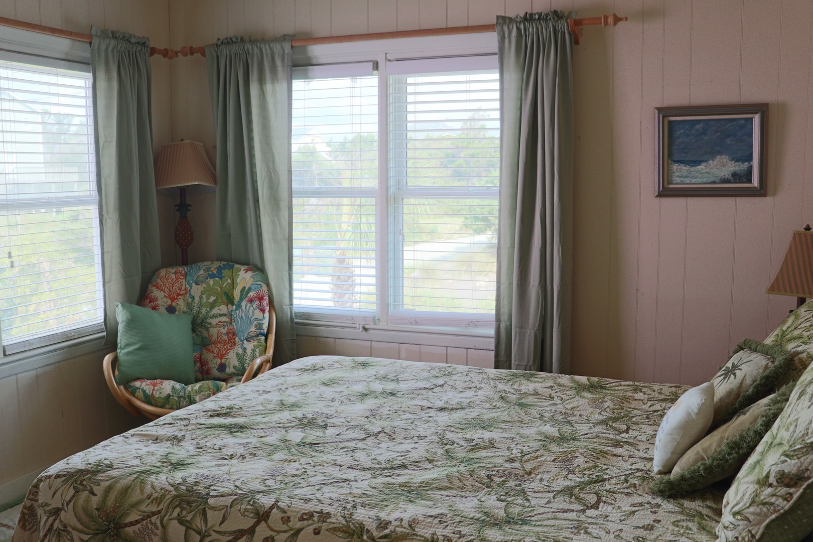 Your peaceful bedroom features tropical bedding and a cozy reading chair by windows overlooking lush greenery.