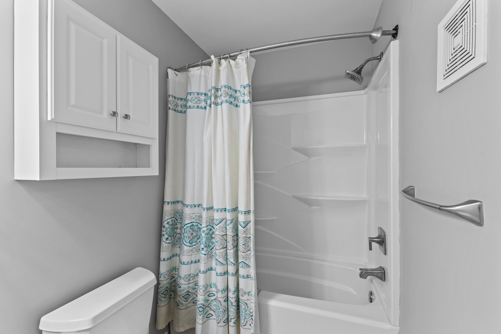 Your private bathroom features a full tub-shower combo with decorative curtain and ample storage in crisp white cabinetry.