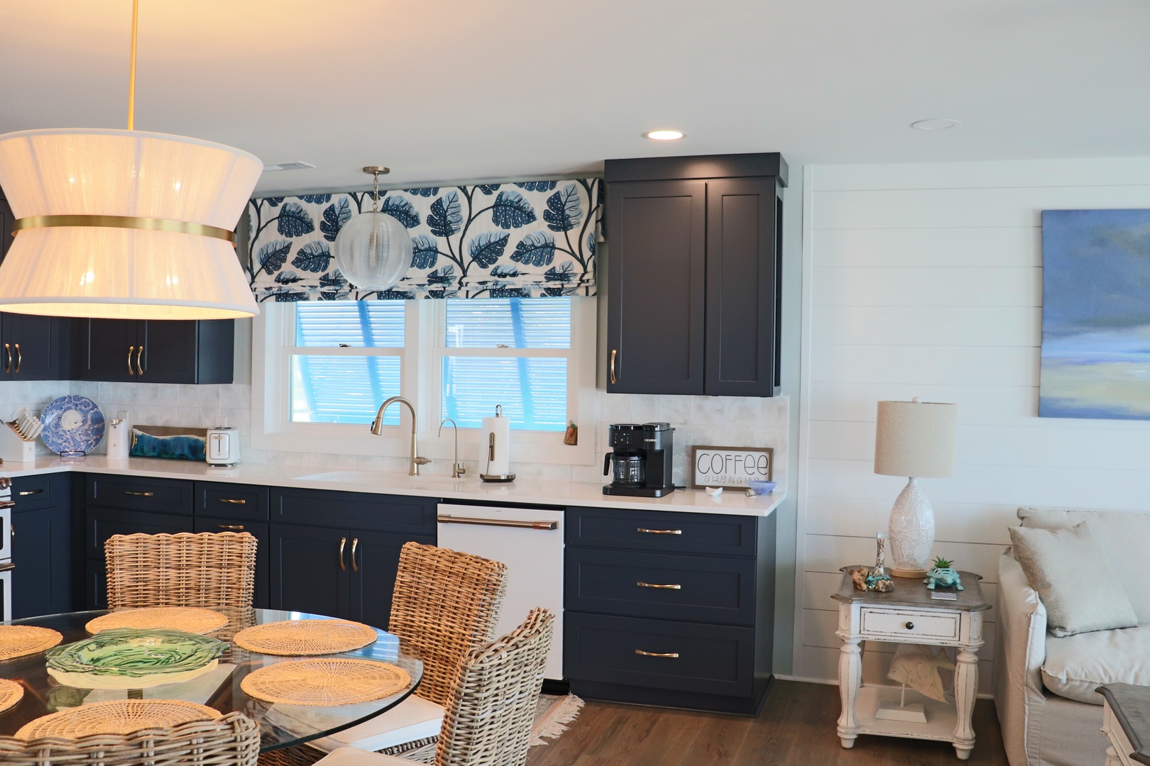 Your stylish coastal kitchen features navy cabinets, wicker dining chairs, and cheerful blue botanical curtains for memorable vacation meals.