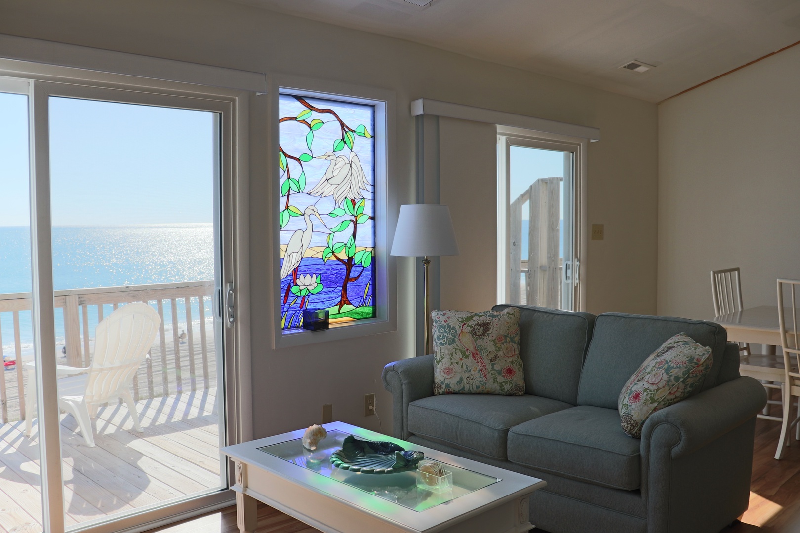 Relax in your bright coastal living room with stunning ocean views and beautiful stained glass artwork creating a peaceful atmosphere.