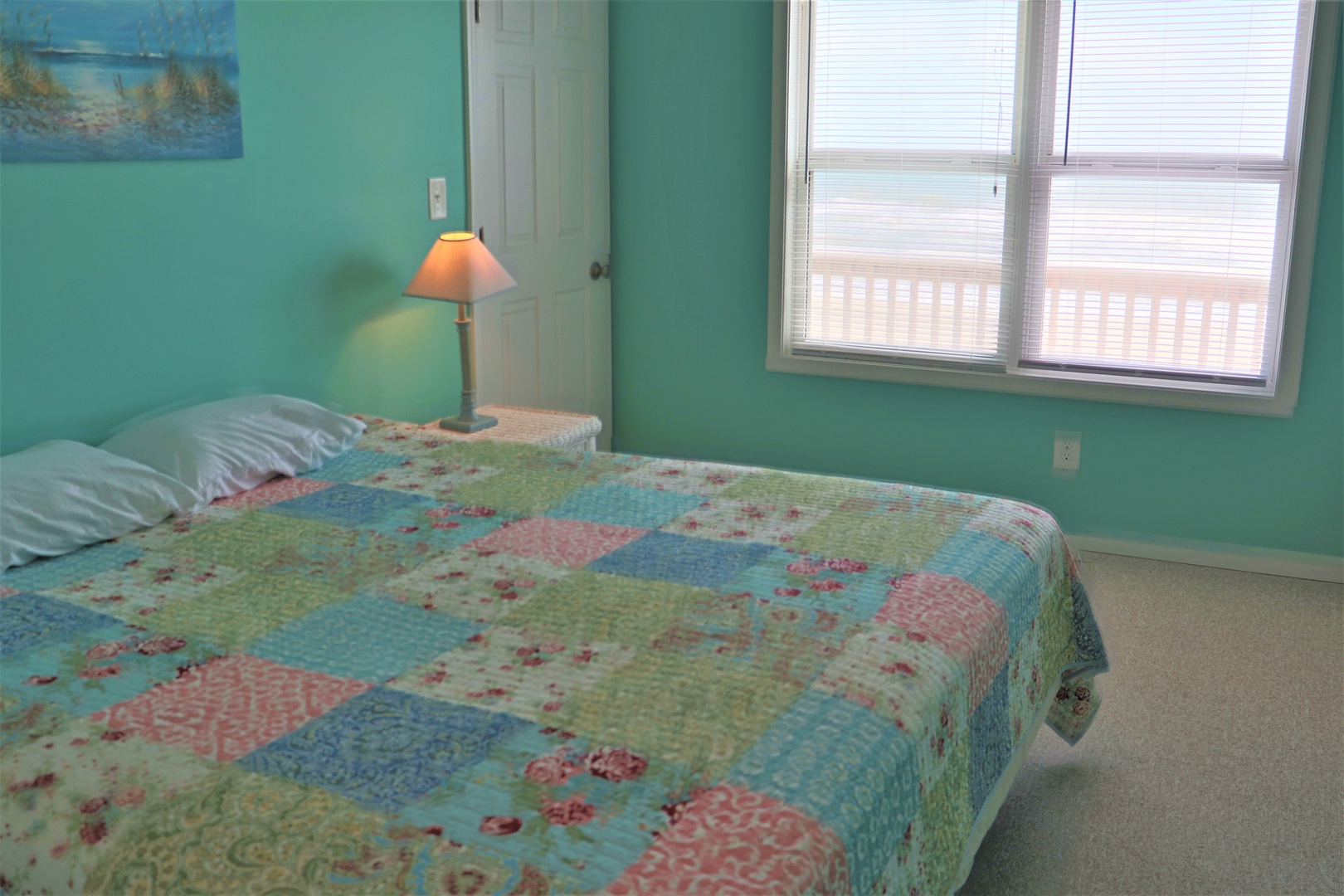 Drift off in this peaceful bedroom with soft turquoise walls and charming patchwork quilt. Natural light fills your space through large windows.