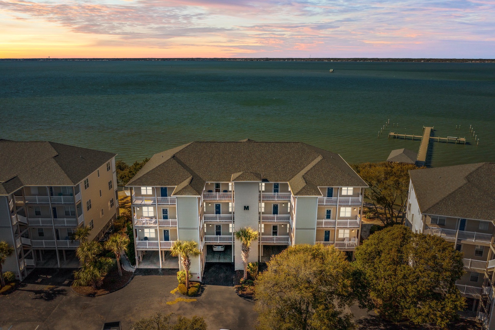 Waterfront property complex showcasing multiple buildings with balconies positioned directly along the scenic coastline at sunset.
