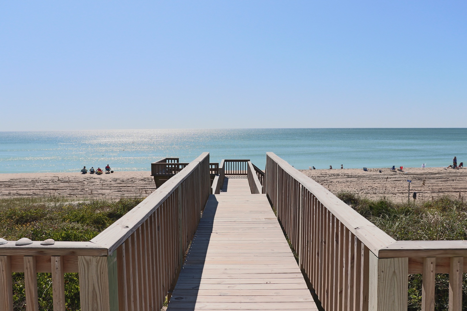 Wooden boardwalk leads to pristine sandy beach and turquoise waters, with beach access and stunning coastal views nearby.
