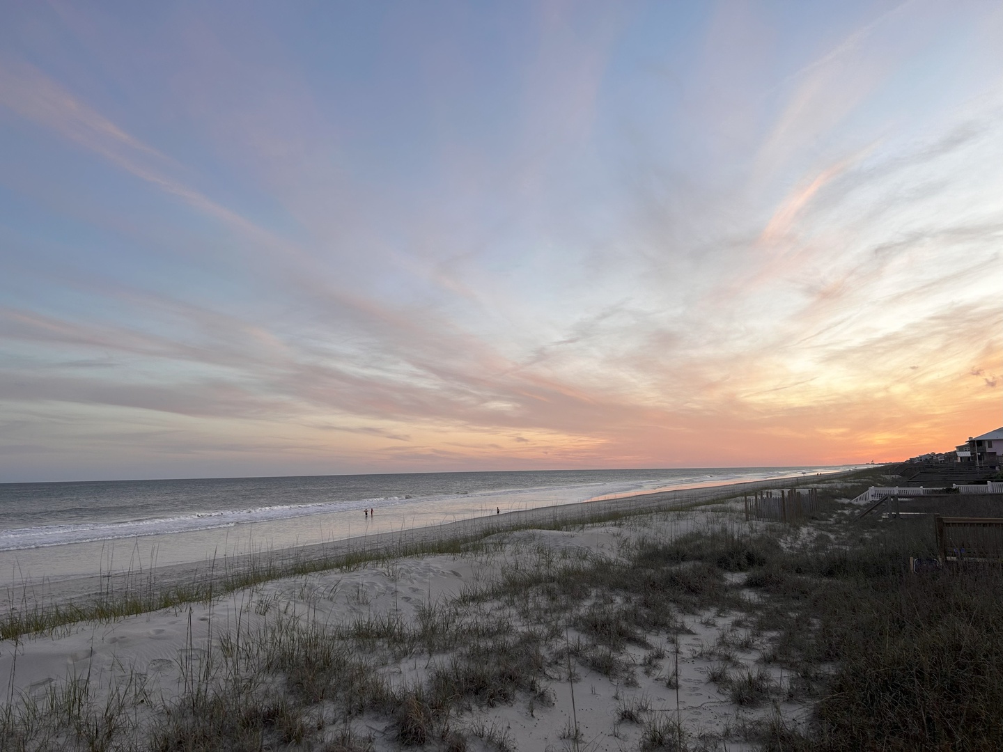 Breathtaking sunset paints the sky in soft pastels over pristine beach with gentle waves and coastal dunes nearby.