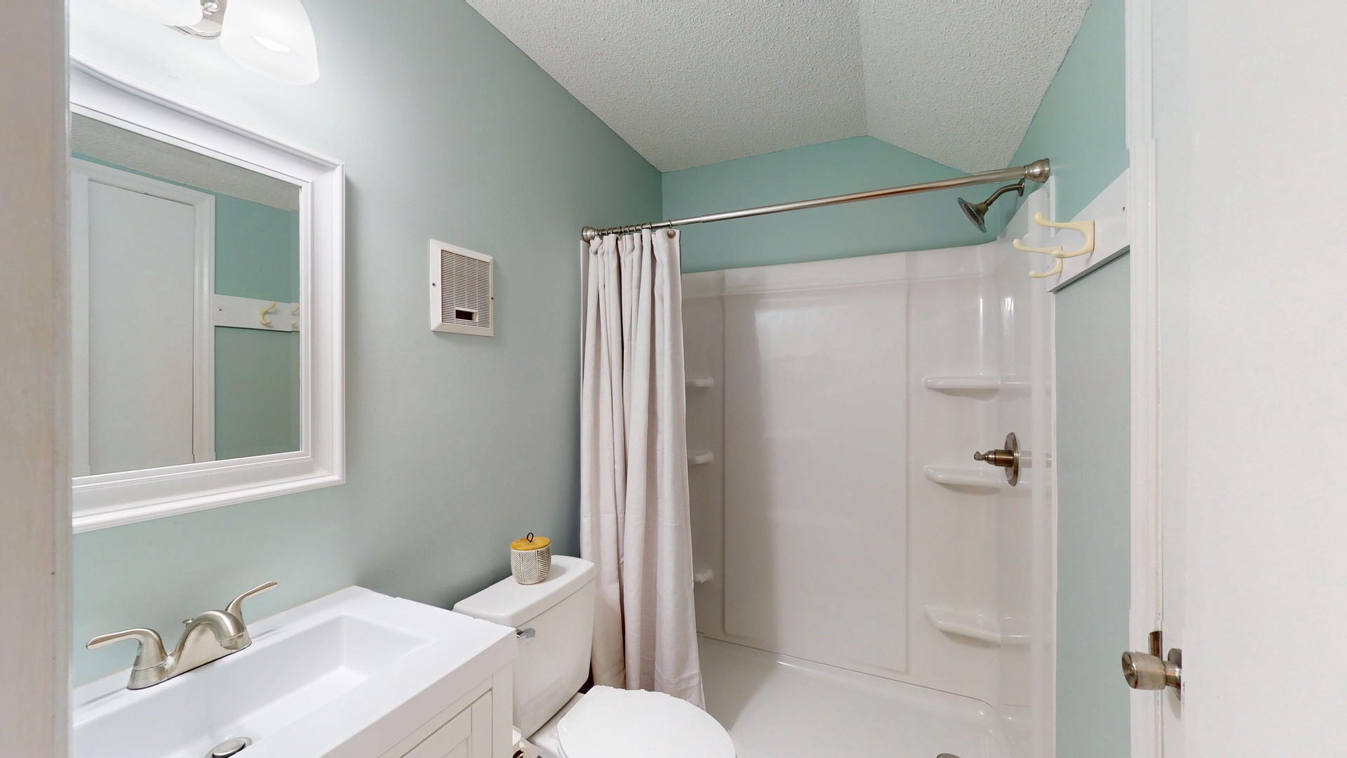 Step into your serene bathroom retreat with soothing mint walls, pristine white fixtures, and a spacious shower waiting for your refreshing moments.