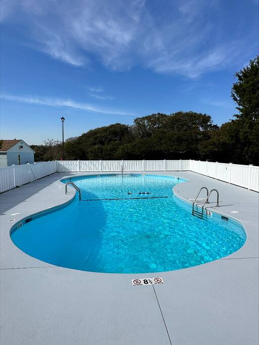 Dive into crystal-clear waters in your private pool oasis, surrounded by white fencing for complete privacy under brilliant blue skies.
