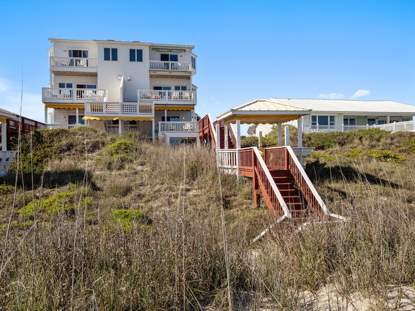 Coastal vacation homes featuring multiple balconies and private beach access via wooden stairs through natural dunes.