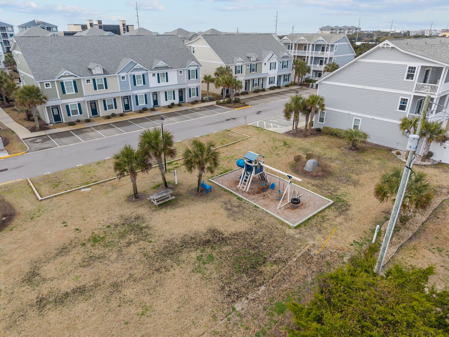 Aerial view of coastal vacation rental community featuring playground and tropical landscaping with palm trees throughout the property grounds.