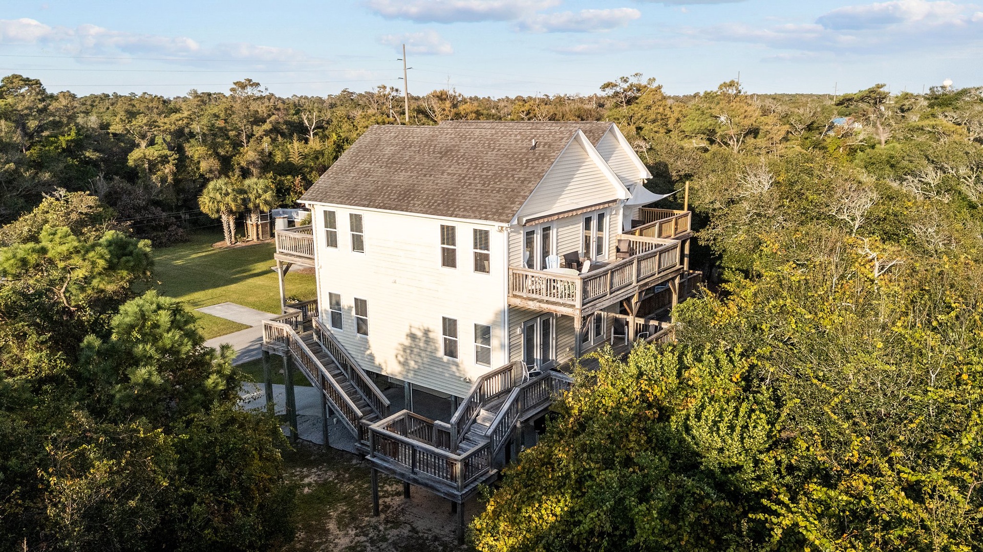 Elevated vacation home nestled among lush coastal trees with wraparound decks and peaceful natural surroundings.