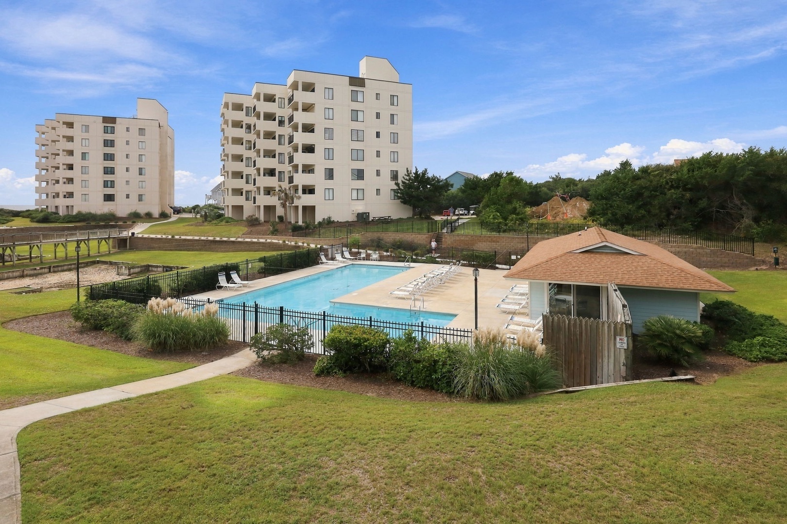 This beachside community features a sparkling outdoor pool surrounded by expansive lawns and lush coastal landscaping, with convenient facilities and scenic green spaces framing the horizon.
