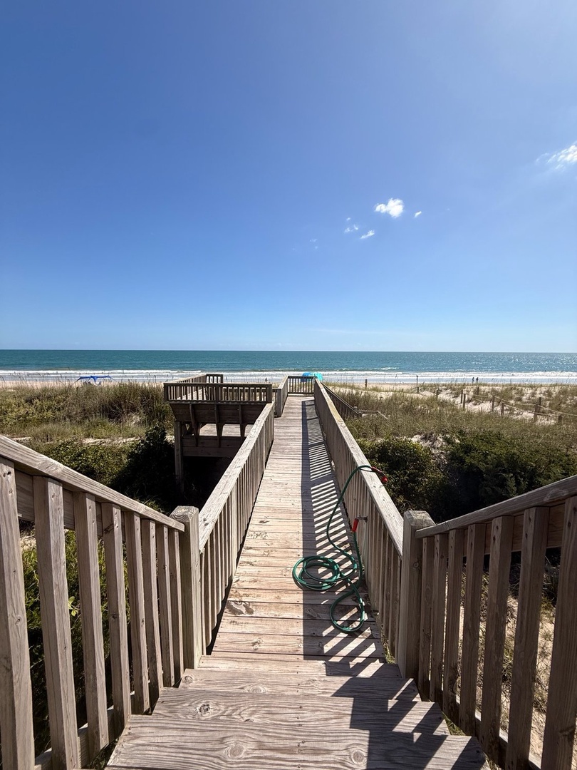 The wooden boardwalk leads through coastal dunes to a private beach deck and pristine sandy shores, with the sparkling ocean just steps away.