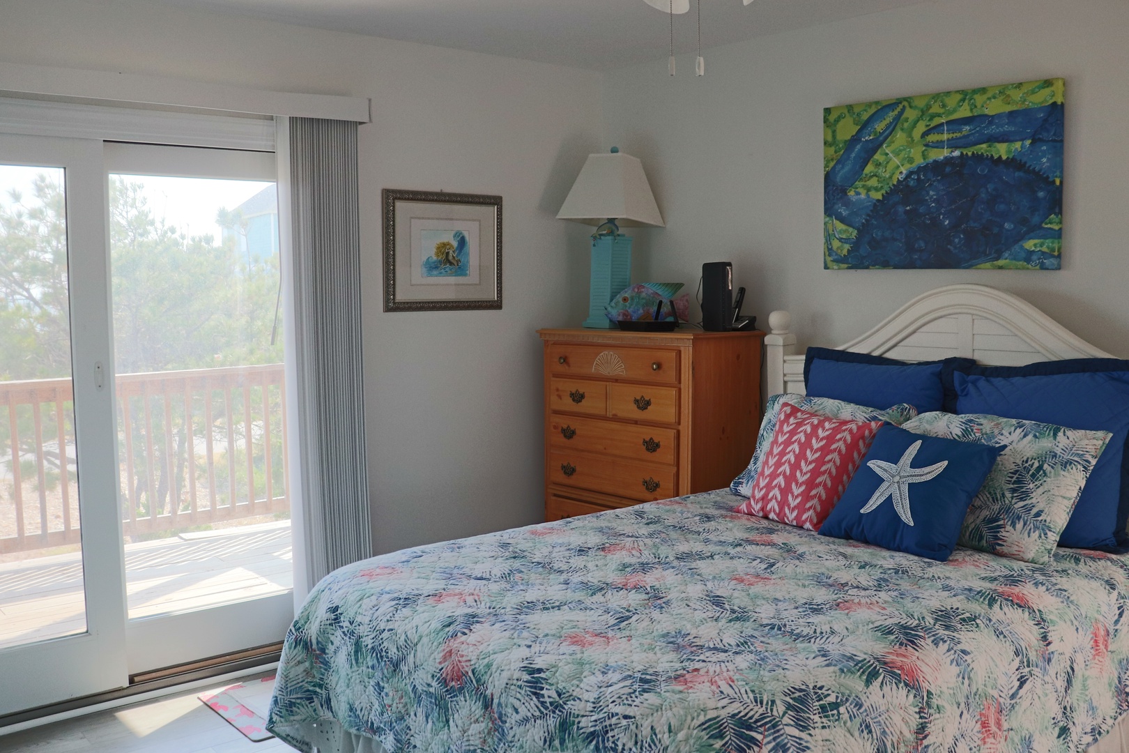 Wake up to coastal charm in your bright bedroom with tropical bedding and peaceful balcony views through sliding doors.