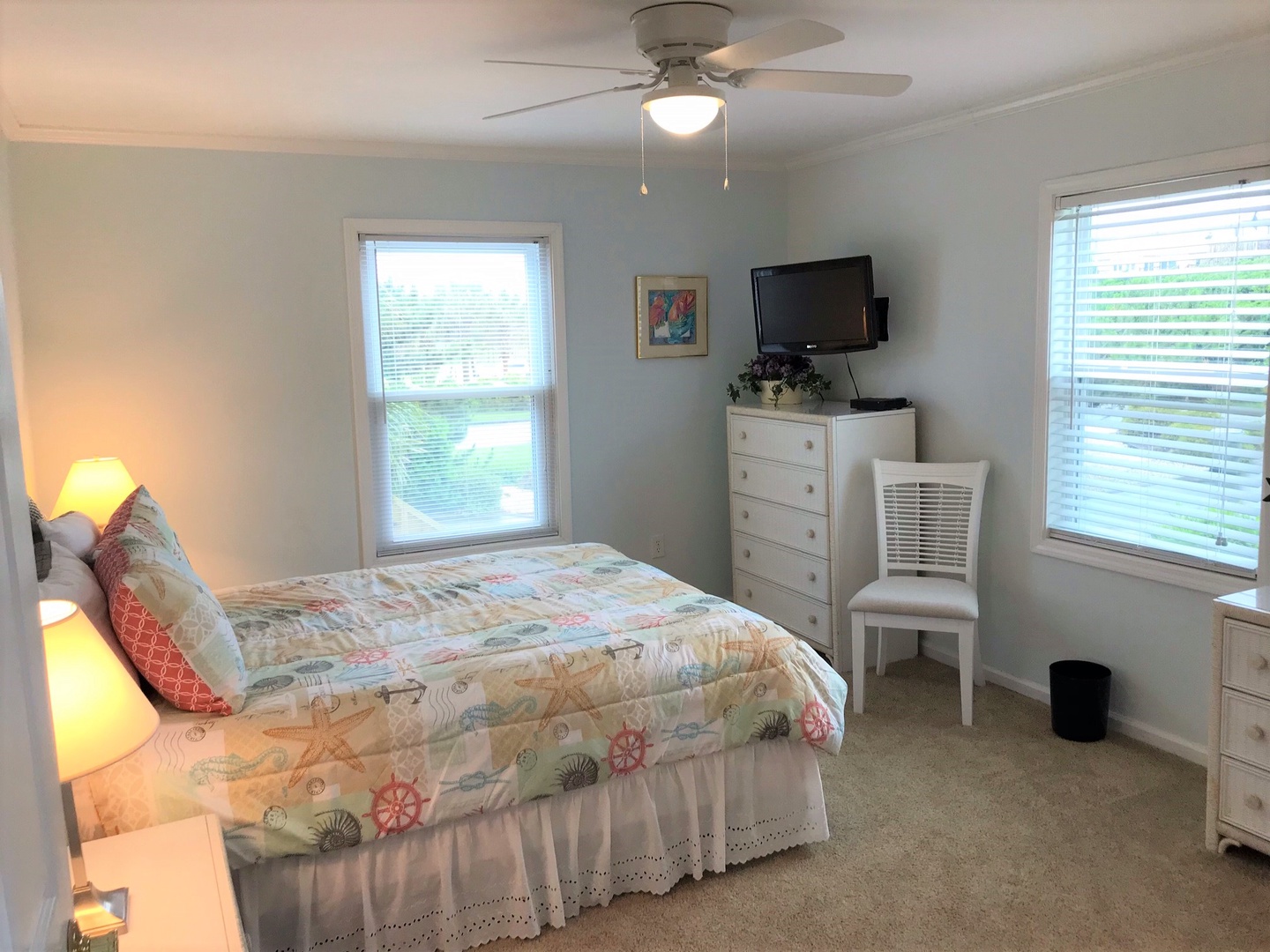 Your bright bedroom features a comfortable bed, flat-screen TV, ceiling fan, and peaceful views through large windows for restful nights.