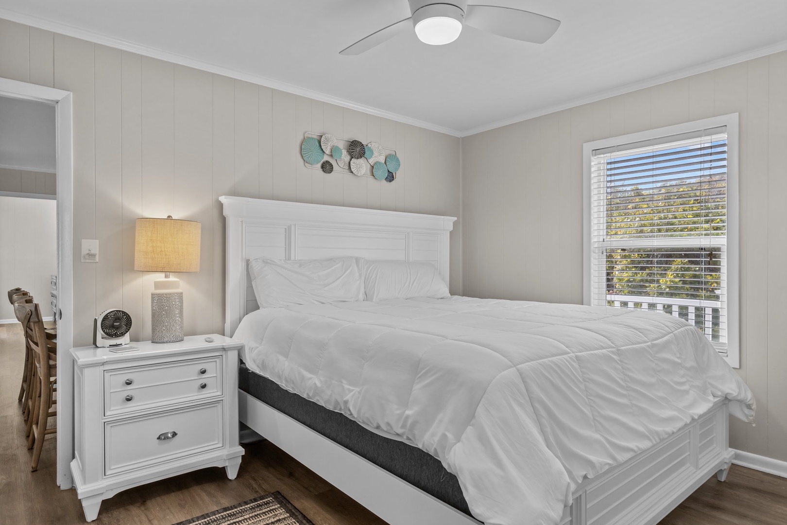 Drift off in this tranquil bedroom featuring a plush bed, soft coastal decor, and refreshing ceiling fan breeze.