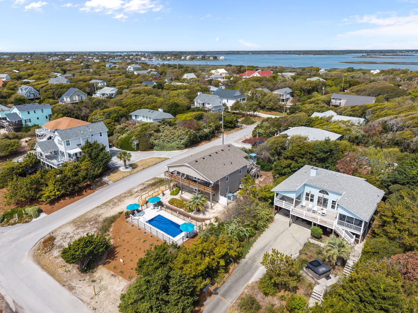 Aerial view of coastal vacation rental properties with private swimming pool, surrounded by lush vegetation near pristine waterfront.