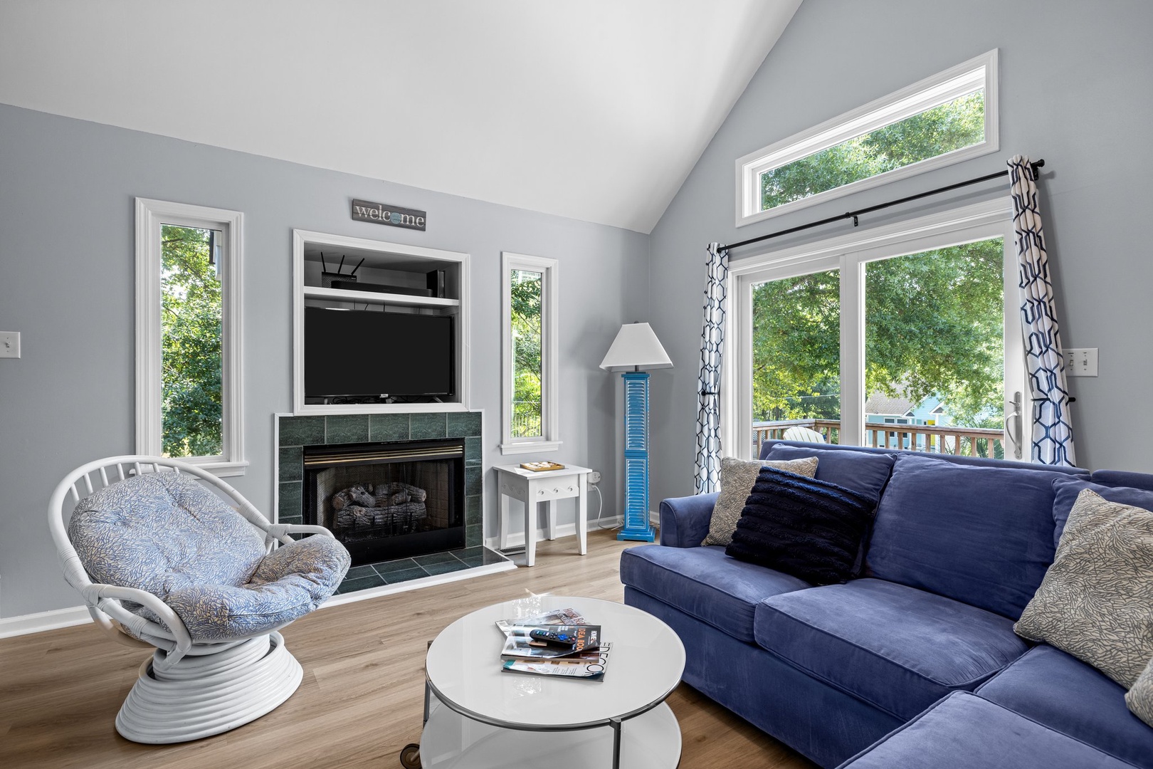 Sink into your plush blue sofa while the fireplace crackles nearby. Natural light floods through windows overlooking leafy surroundings.