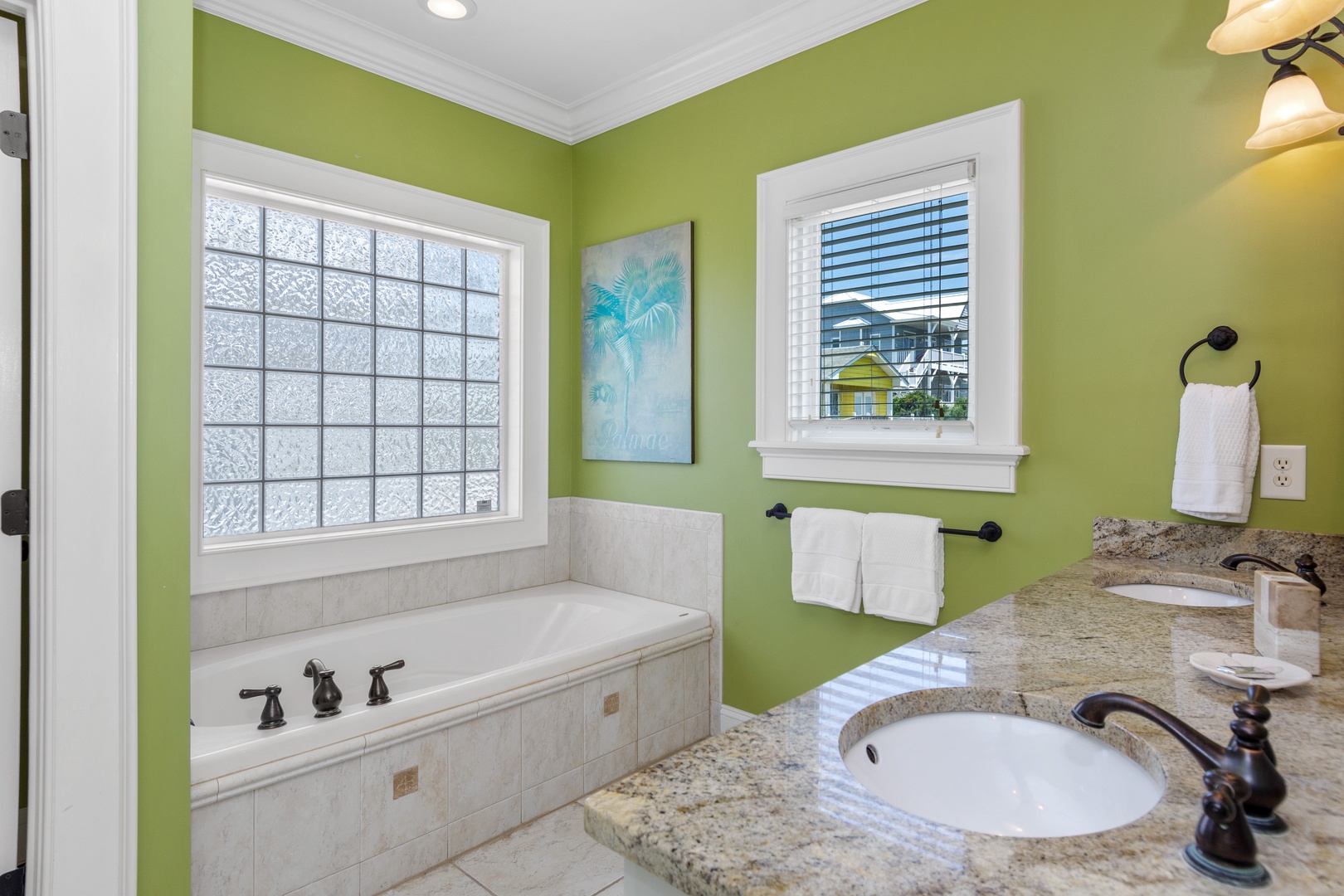 Unwind in your elegant spa-like bathroom featuring a deep soaking tub, dual vanities with granite countertops, and cheerful tropical décor.