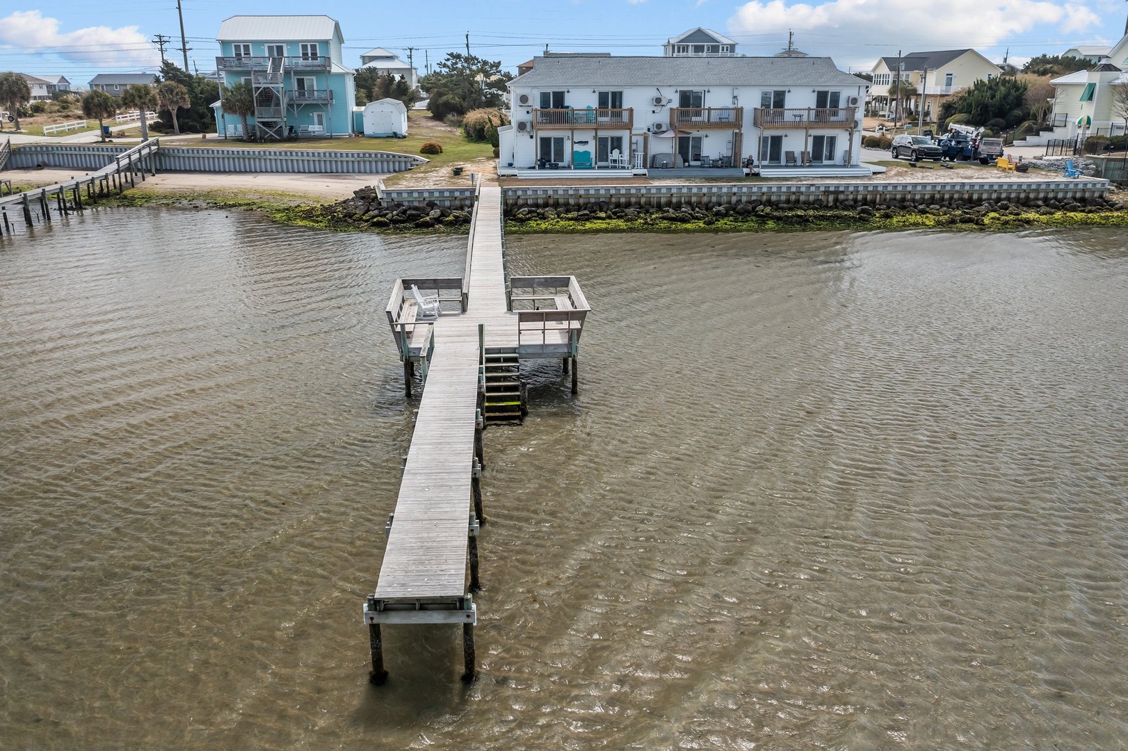 Waterfront property with private dock extending into calm bay waters, surrounded by coastal neighborhood homes.