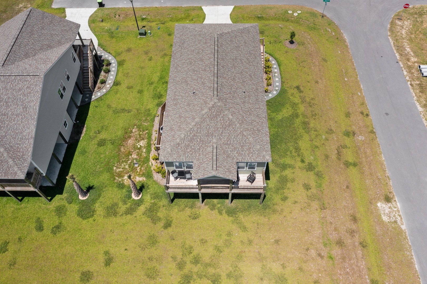 Aerial view of a modern vacation rental home featuring a welcoming deck area and manicured landscaping in a quiet residential neighborhood.