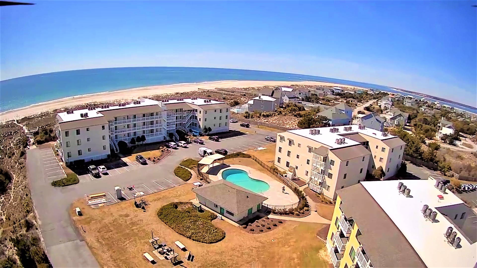 Aerial view of beachfront resort complex with swimming pool, multiple buildings, and pristine sandy beach stretching along the coastline.