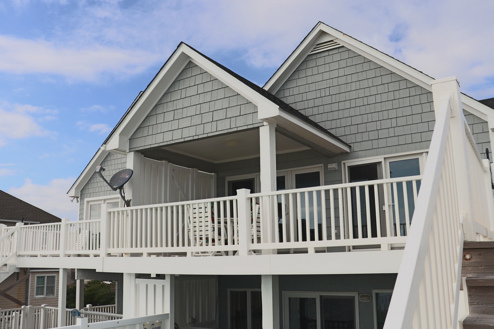 Charming coastal-style property with classic gray shingle siding and white trim, featuring spacious covered decks perfect for relaxing outdoors.