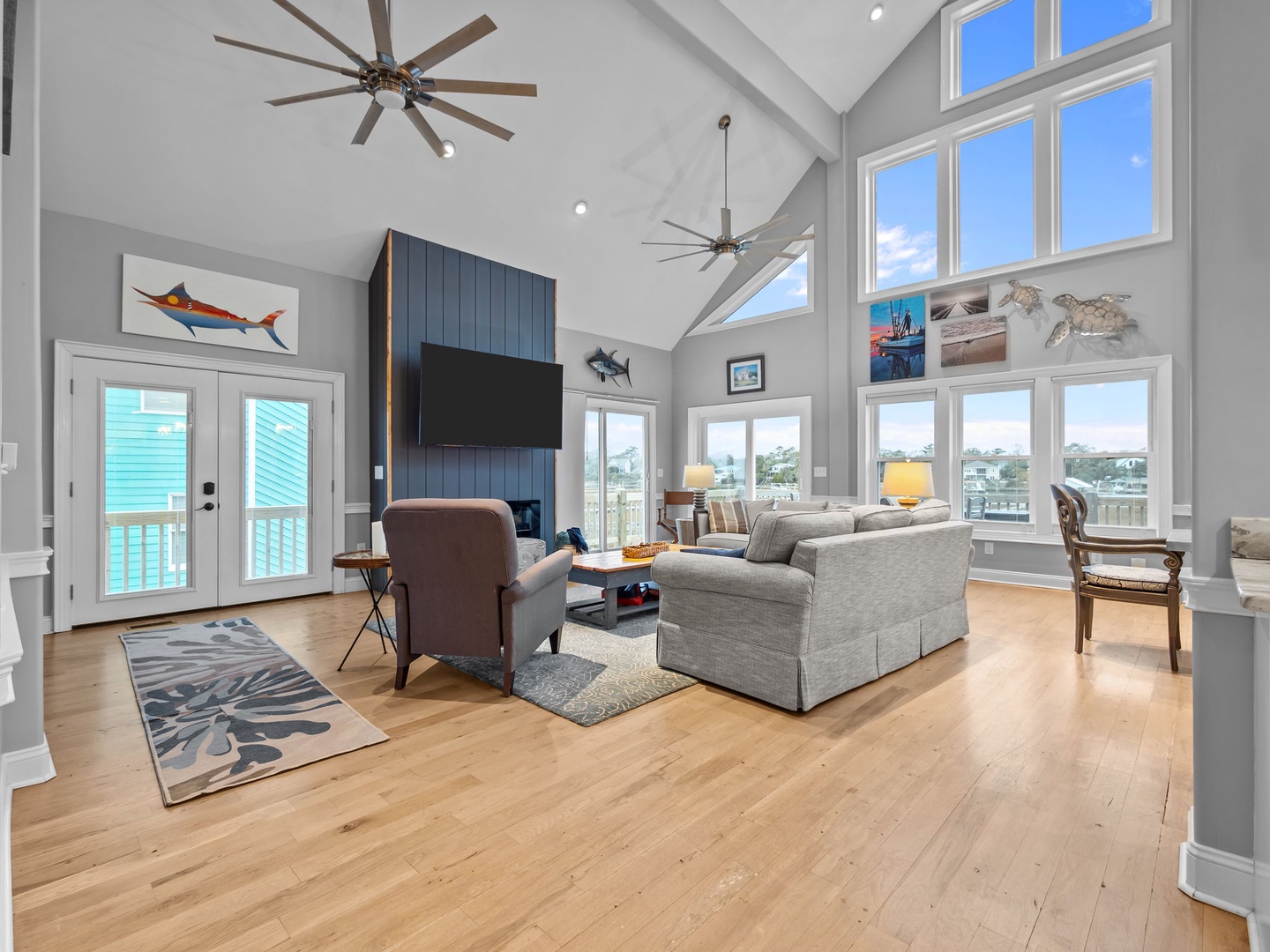 Your coastal living room awaits with vaulted ceilings, ocean artwork, and panoramic water views through floor-to-ceiling windows.