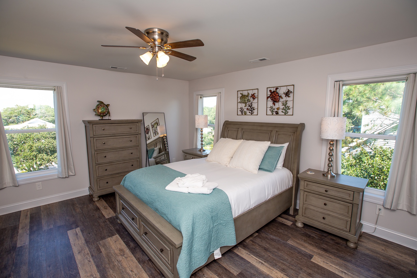 Sink into your plush bed surrounded by calming teal accents and natural light streaming through large windows overlooking peaceful greenery.
