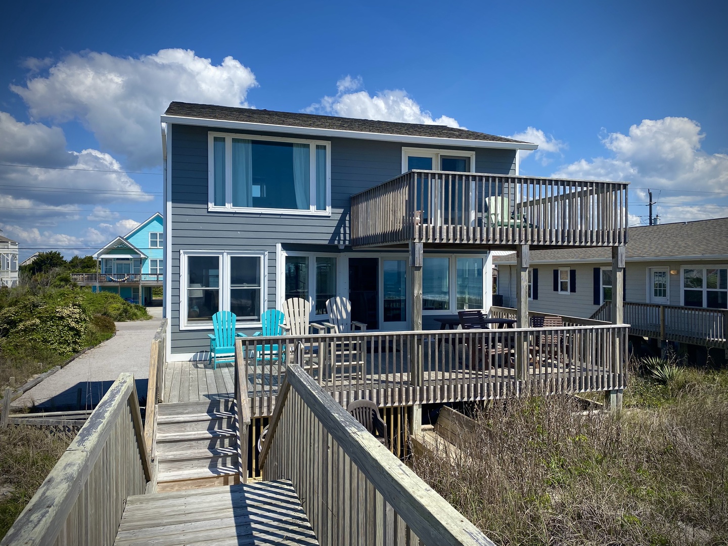 A charming coastal retreat with multi-level decks and colorful Adirondack chairs, positioned steps from the beach via private walkway.