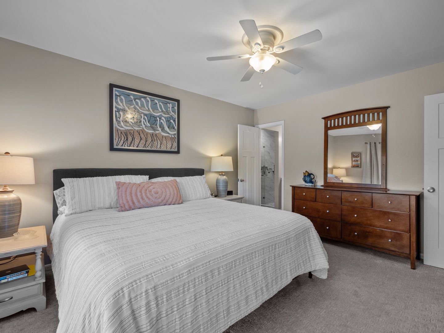 Unwind in your spacious bedroom featuring a plush king bed, warm wood dresser, and gentle ceiling fan for perfect comfort.