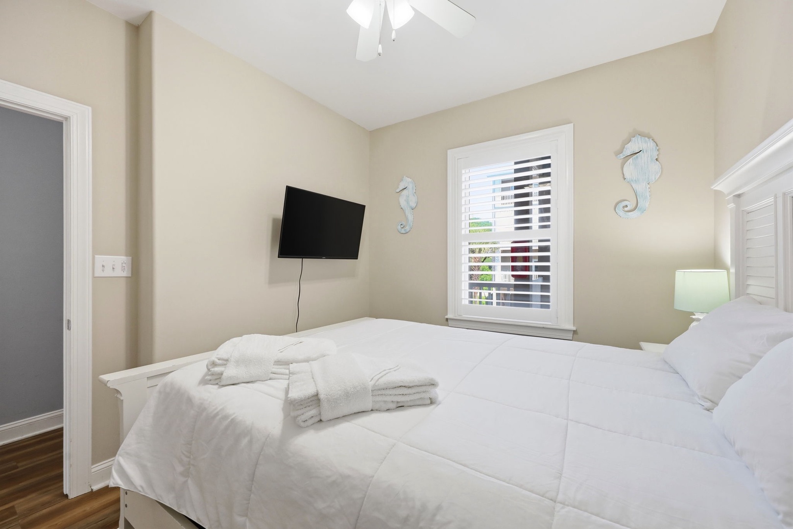 Your serene coastal bedroom features plush linens, a mounted TV, and charming seahorse accents. Natural light filters through plantation shutters, creating a peaceful retreat for restful nights.