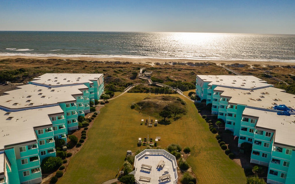 Oceanfront resort buildings positioned perfectly between pristine beach and open green spaces, creating an ideal coastal getaway location.