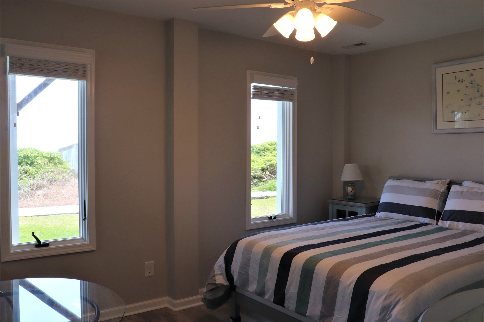 Unwind in your peaceful bedroom with garden views, striped linens, and a ceiling fan for comfort.
